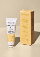 Osmology Hand Therapy Hand Cream in a white and yellow tube next to its yellow packaging box, labeled 'Mayan Vanilla', on a neutral beige background.